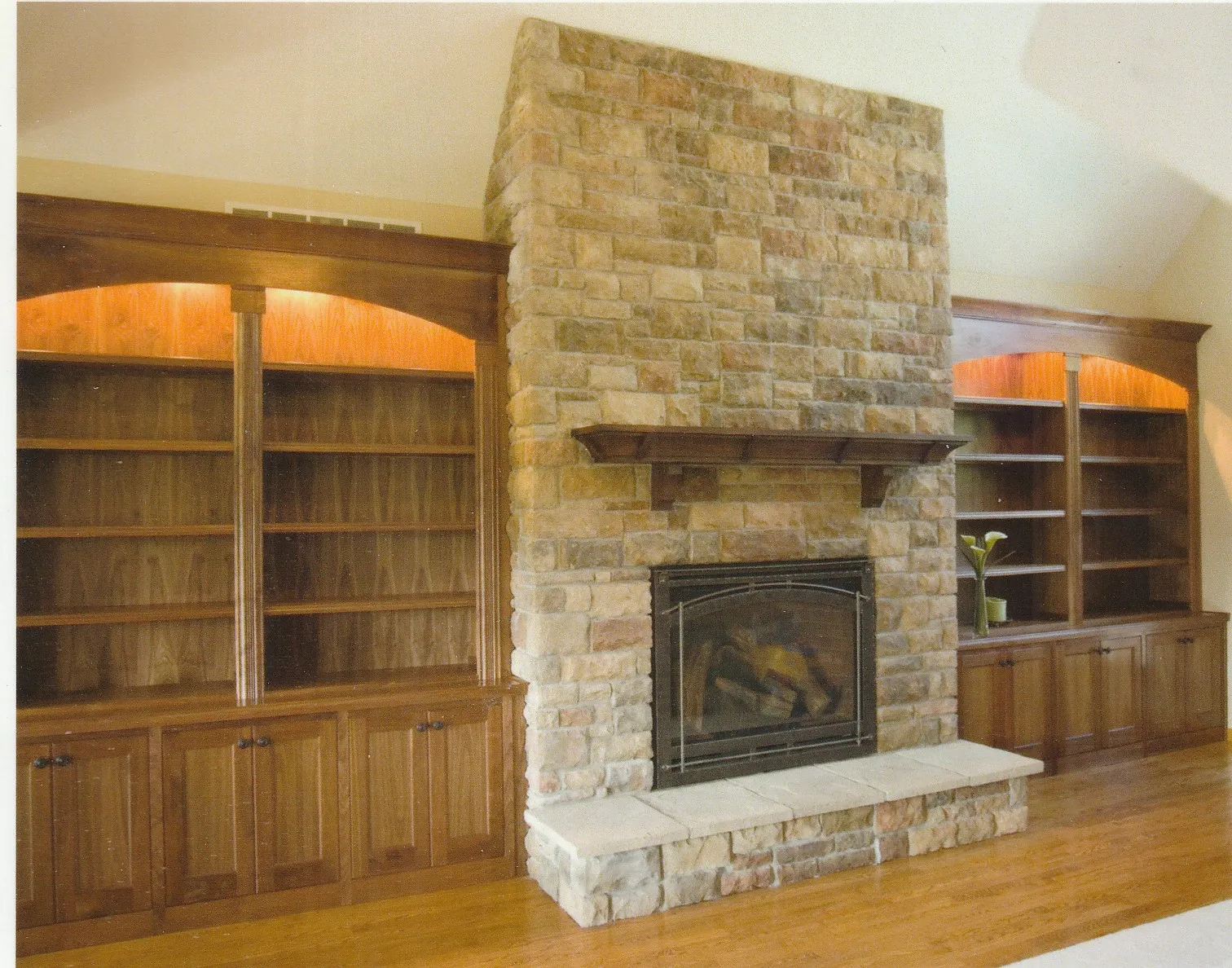 Cozy living room featuring a stone fireplace with a wooden mantel, flanked by built-in wooden bookshelves with soft lighting